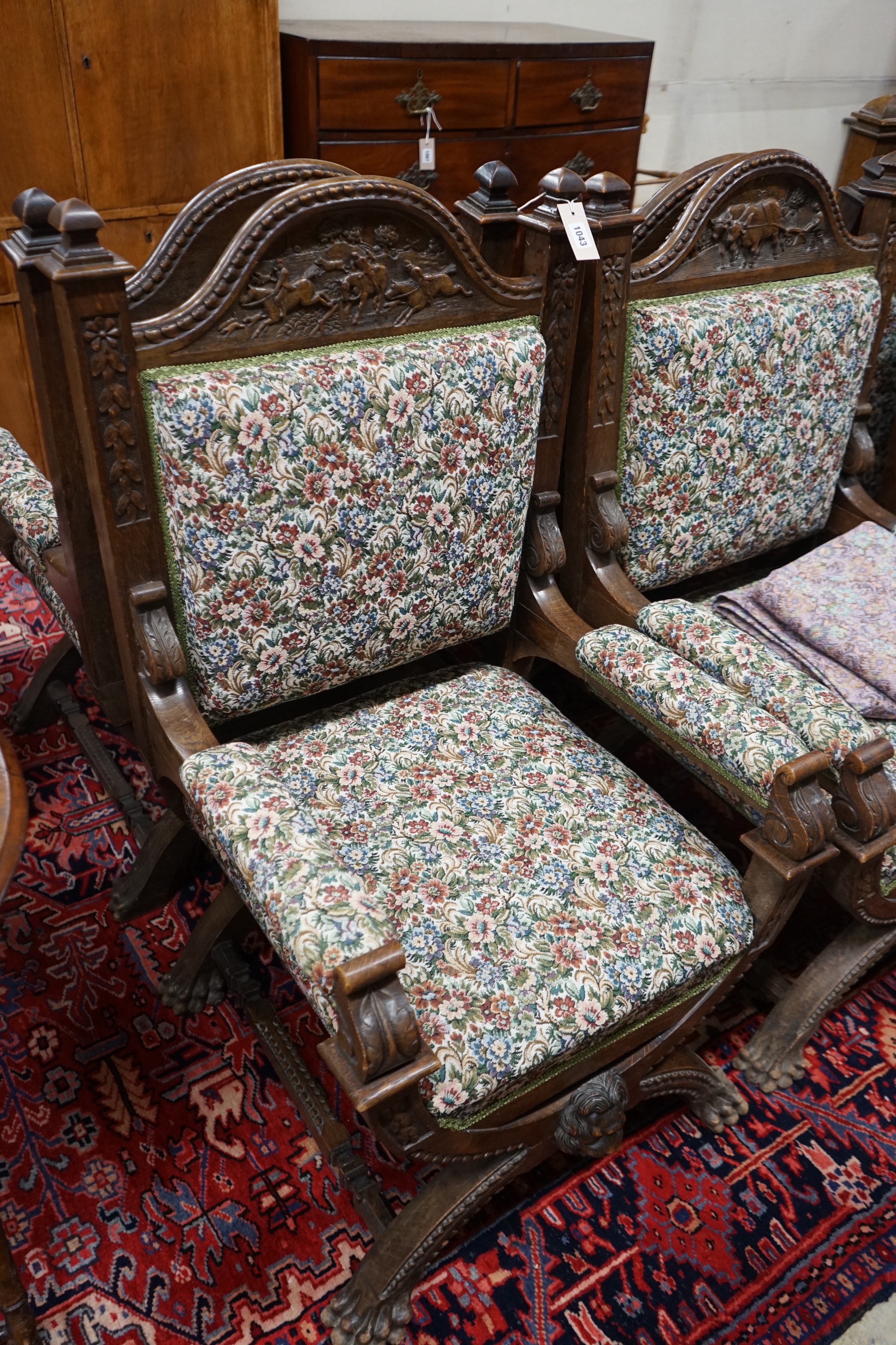Seven (6+1) early 20th century carved oak upholstered X frame elbow chairs, largest width 75cm, depth 62cm, height 114cm